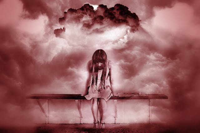 Junge Frau die auf einer Bank übergebeugt sitzt und in eine Tiefe zu schauen scheint. Um sie herum sind defuse Wolken zu sehent